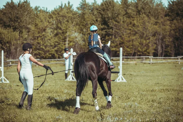 Una niña está aprendiendo a montar a caballo.. — Foto de Stock
