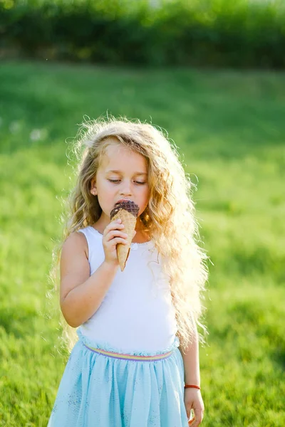 Little blonde girl with long hair has fun eating ice cream in a summer park.