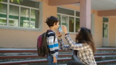 Anne oğluna okula kadar eşlik eder. Bir anne okula girmeden önce oğlu için koruyucu bir maske takar. Okul yılının başlangıcı..