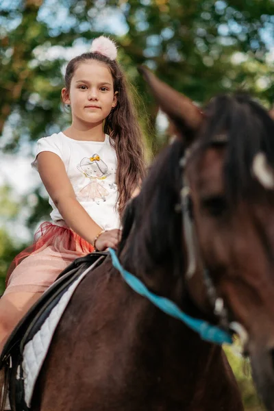 Little blonde girl with long hair rides a horse in the park at sunset in autumn. Autumn horse ride. Friendship of a girl and a horse. — Stock Photo, Image