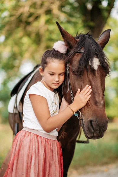 L'amitié d'un enfant avec un cheval. Une petite fille caresse affectueusement son cheval. Promenades avec un cheval dans le parc en automne. — Photo