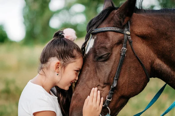 Freundschaft eines Kindes mit einem Pferd. Ein kleines Mädchen streichelt liebevoll ihr Pferd. Wandermädchen mit Pferd im Herbst im Park. — Stockfoto