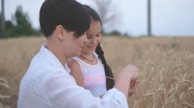 Anne ve küçük kızı yazın tarlada yürüyorlar. Anne ve çocuk tarladaki buğday tanelerini inceliyor. Aile yaz yürüyüşü buğday tarlasında.