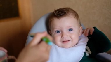 Tatlı bebek yemek yemek istemiyor. Küçük bir çocuk çocuk sandalyesine oturur ve yemek yemeyi reddeder. Anne bebeği kaşıkla besler, ama bebek yemek istemez..