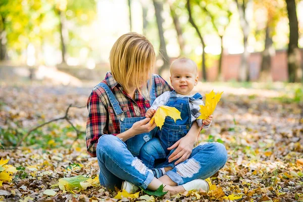 stock image Happy young mother playing with baby in autumn park with yellow maple leaves. Family walking outdoors in autumn. Little boy with her mother playing in the park in autumn.