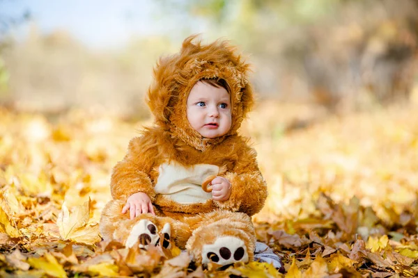 Kid in a lion costume plays in the yellow autumn leaves in the park. Cheerful and happy childhood of the kid.