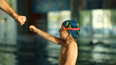 Antrenörün havuzdaki küçük sporcu yüzücüyle başarısı ve etkileşimi. Küçük bir sporcu çocuk koça yumruğuyla vuruyor..