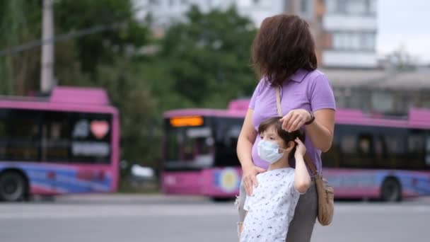 一对母子站在公交车站等公共汽车。城市中的大范围的大肠癌病毒covid-19 。人们都戴着防护面具等公共交通工具. — 图库视频影像