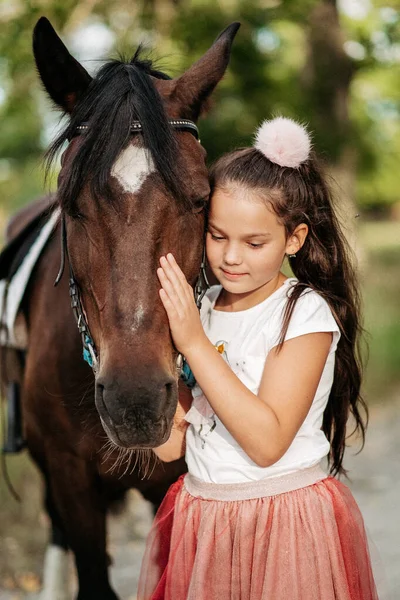 L'amitié d'un enfant avec un cheval. Une petite fille caresse affectueusement son cheval. Promenades avec un cheval dans le parc en automne. — Photo