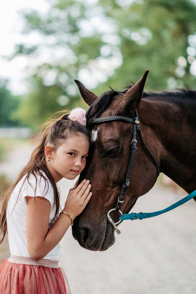 Дружба ребенка с лошадью. Маленькая девочка ласково гладит свою лошадь. Прогулочные девушки с лошадью в парке осенью.