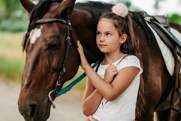L'amitié d'un enfant avec un cheval. Une petite fille caresse affectueusement son cheval. Promenades avec un cheval dans le parc en automne. — Photo