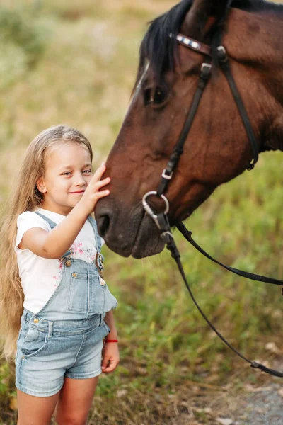 Przyjaźń dziecka z koniem. Mała dziewczynka pieszczotliwie głaszcze swojego konia. Spacerujące dziewczyny z koniem w parku jesienią. — Zdjęcie stockowe
