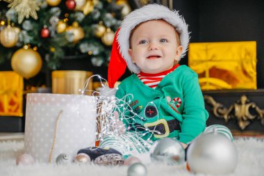 Elf gibi giyinmiş şirin bir çocuk Noel hediyesini süslü bir Noel evinde açıyor..