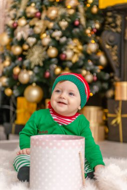 Elf gibi giyinmiş şirin bir çocuk Noel hediyesini süslü bir Noel evinde açıyor..