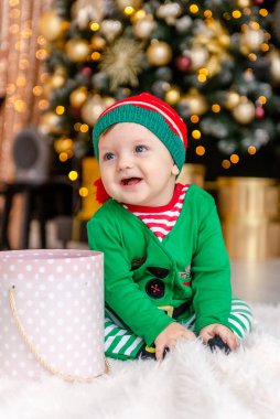 Elf gibi giyinmiş şirin bir çocuk Noel hediyesini süslü bir Noel evinde açıyor..