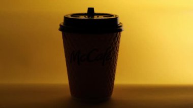 Masanın üzerinde sarı bir McCoffee bardağı duruyor. Bardağın aydınlatma düzgünce değişiyor. Düzenleyici video.