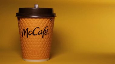 Masanın üzerinde sarı bir McCoffee bardağı duruyor. Bardağın aydınlatma düzgünce değişiyor. Düzenleyici video.
