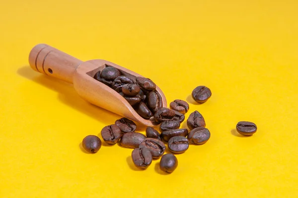 Kahve kaşığındaki kahve çekirdekleri sarı arka plana saçılmış..