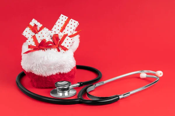 Noel Baba çanta dolusu hediyeyle dolu kırmızı arka planda steteskop ve fotokopi alanı. Tıp konsepti.