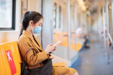 Trende, koruyucu maske takan Asyalı bir kadın Covid19 akıllı telefon kullanıyor..