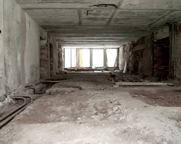 The perspective of a large empty room with broken windows in an abandoned building.