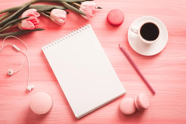 ?Kahve, makarna, ofis malzemeleri ve pembe pastel masa manzaralı boş bir defter. Düz yatış stili. Güzel bir sabah kahvaltısı. Moda kadın blog yazarı çalışma masasında.
