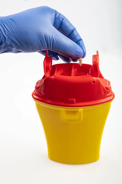 Health worker throws sharp waste into the medical waste bin. Medical waste bin pocket size 0,4 liter. Yellow biohazard medical contaminated clinical waste container isolated on white background.