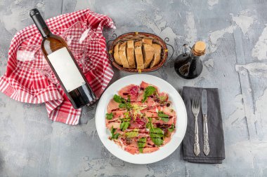 Carpaccio bifteği, şarap, kapari ve roka ile birlikte beyaz tabakta soğuk meze..