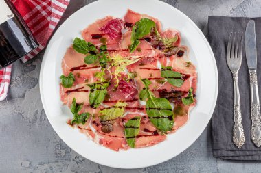 Carpaccio bifteği, şarap, kapari ve roka ile birlikte beyaz tabakta soğuk meze..