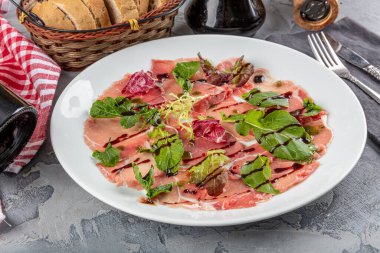 Carpaccio bifteği, şarap, kapari ve roka ile birlikte beyaz tabakta soğuk meze..