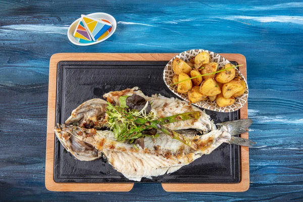 Grilled sea bass on the wooden board. Grilled sea bass served on a plate with various sauces and decorated with parsley and lemon.