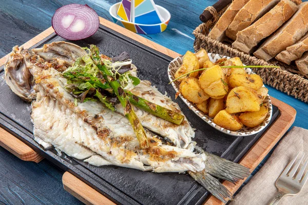 Grilled sea bass on the wooden board. Grilled sea bass served on a plate with various sauces and decorated with parsley and lemon.