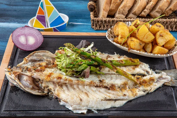 Grilled sea bass on the wooden board. Grilled sea bass served on a plate with various sauces and decorated with parsley and lemon.