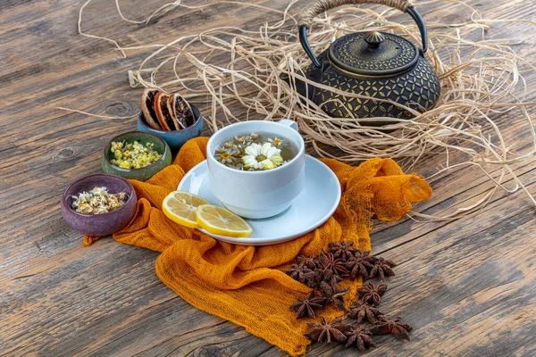 Chamomile tea in cast teapot. Chamomile tea cup, antique chinese cast iron teapot, lemon and star anise on a wooden table.