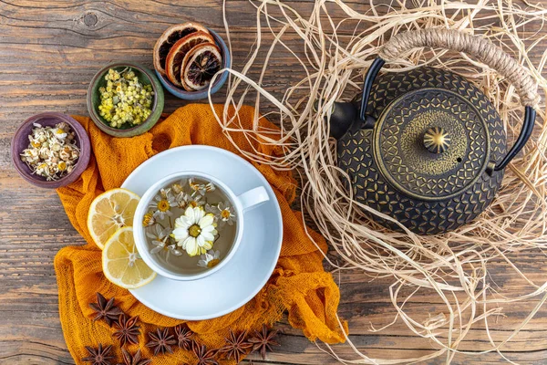 Chamomile tea in cast teapot. Chamomile tea cup, antique chinese cast iron teapot, lemon and star anise on a wooden table.