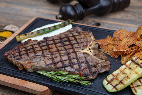 Barbecued t-bone steak seasoned with fresh herbs and marinade served with a cutting board in a steakhouse. Delicious restaurant food