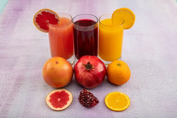 Glassware with refreshing citrus fruits cocktail on white wooden background. Antioxidant juices of Pomegranate Juice, Orange Juice, Grapefruit Juice.
