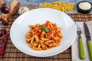 Acı soslu arrabiata soslu makarna. Klasik İtalyan penne arrabiata fesleğenli ve taze rendelenmiş pecorino peynirli ahşap masa..