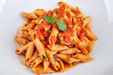 Acı soslu arrabiata soslu makarna. Klasik İtalyan penne arrabiata fesleğenli ve taze rendelenmiş pecorino peynirli ahşap masa..