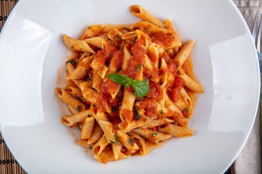 Acı soslu arrabiata soslu makarna. Klasik İtalyan penne arrabiata fesleğenli ve taze rendelenmiş pecorino peynirli ahşap masa..