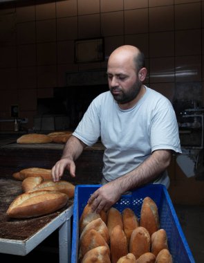 Fırında çalışan genç bir erkek işçi. O, ekmeği rafa koyar. Fırından taze somun ekmeği. Ekmek pişiriyorum. Fırın Taşımacılığı.