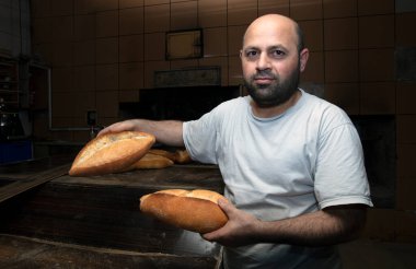 Fırında çalışan genç bir erkek işçi. O, ekmeği rafa koyar. Fırından taze somun ekmeği. Ekmek pişiriyorum. Fırın Taşımacılığı.