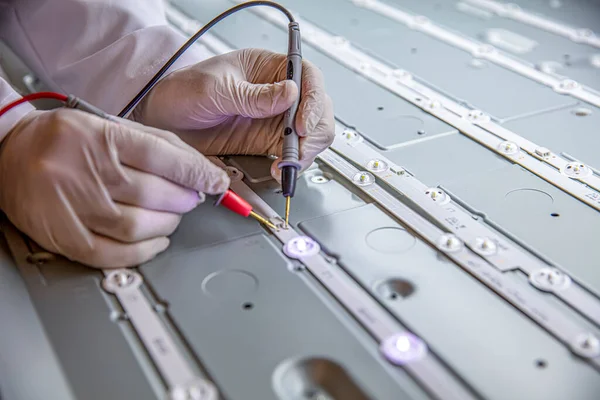 Repair of led television with digital multimeter, control of led strips. The engineer measures the voltage on the LED board with a multimeter. Repair LED TV, rear panel close-up.