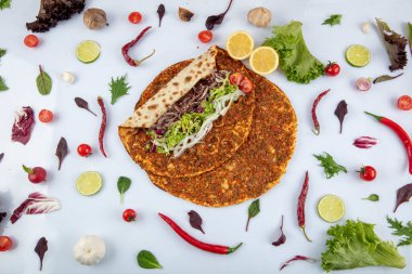Etli, soğanlı ve maydanozlu Lahmacun adı verilen geleneksel Türk pizzası sergileniyor. Beyaz arka planda yeşil sebzeler arasında Türk Lahmacunu. Lahmacun Restoranı konsepti.