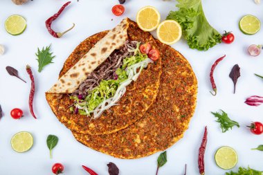 Etli, soğanlı ve maydanozlu Lahmacun adı verilen geleneksel Türk pizzası sergileniyor. Beyaz arka planda yeşil sebzeler arasında Türk Lahmacunu. Lahmacun Restoranı konsepti.