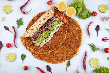 Etli, soğanlı ve maydanozlu Lahmacun adı verilen geleneksel Türk pizzası sergileniyor. Beyaz arka planda yeşil sebzeler arasında Türk Lahmacunu. Lahmacun Restoranı konsepti.