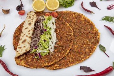 Etli, soğanlı ve maydanozlu Lahmacun adı verilen geleneksel Türk pizzası sergileniyor. Beyaz arka planda yeşil sebzeler arasında Türk Lahmacunu. Lahmacun Restoranı konsepti.