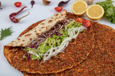 Etli, soğanlı ve maydanozlu Lahmacun adı verilen geleneksel Türk pizzası sergileniyor. Beyaz arka planda yeşil sebzeler arasında Türk Lahmacunu. Lahmacun Restoranı konsepti.