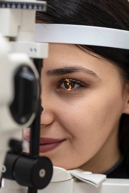 Göz bakımı için yüksek teknoloji konsepti. Göz doktorunun göz kliniğindeki göz doktoru, göz kontrolü için genç bir kadına dürbün lamba kullanıyor.. 