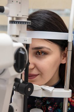 Göz bakımı için yüksek teknoloji konsepti. Göz doktorunun göz kliniğindeki göz doktoru, göz kontrolü için genç bir kadına dürbün lamba kullanıyor.. 